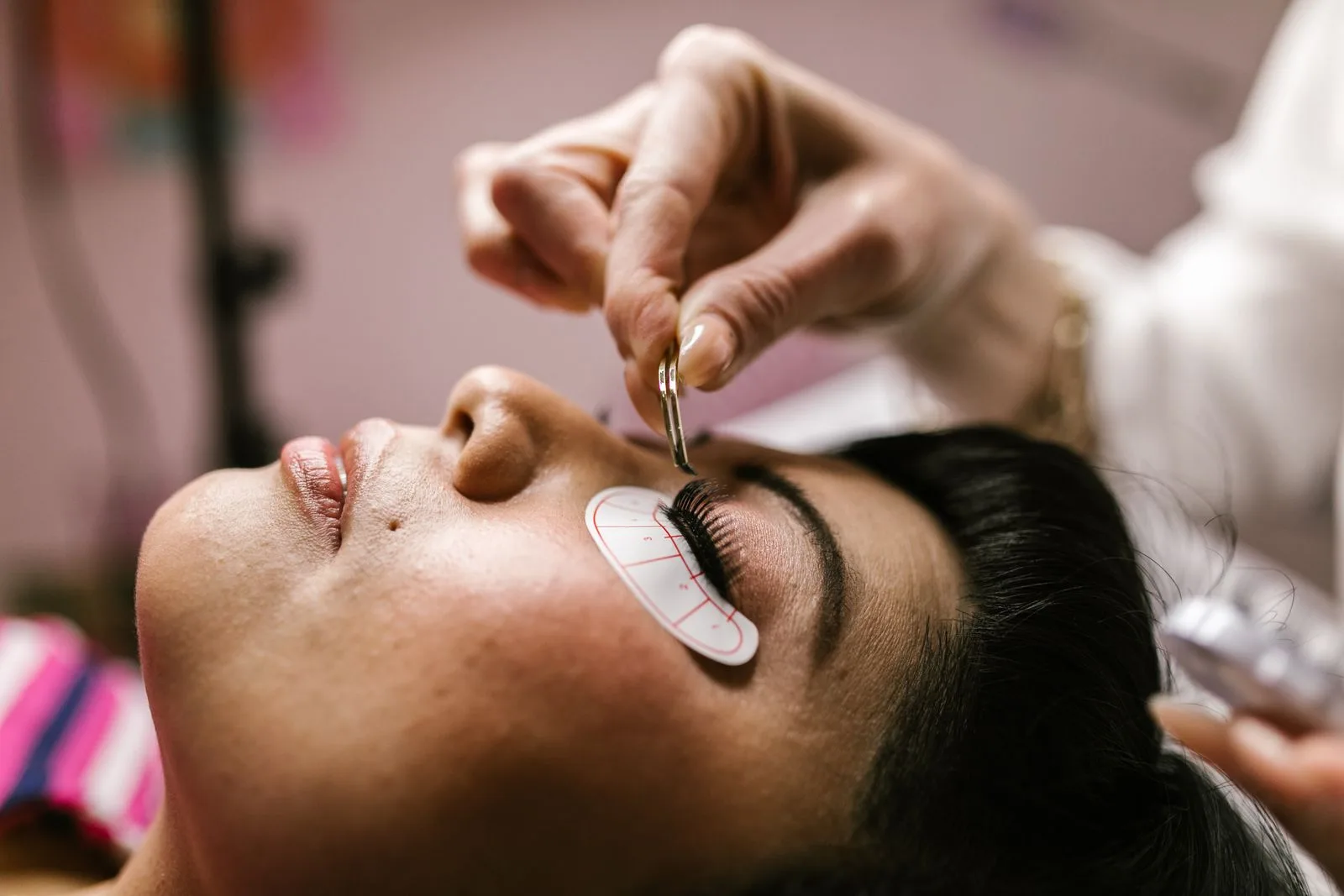 A lash technician working carefully with tweezers during an eyelash treatment