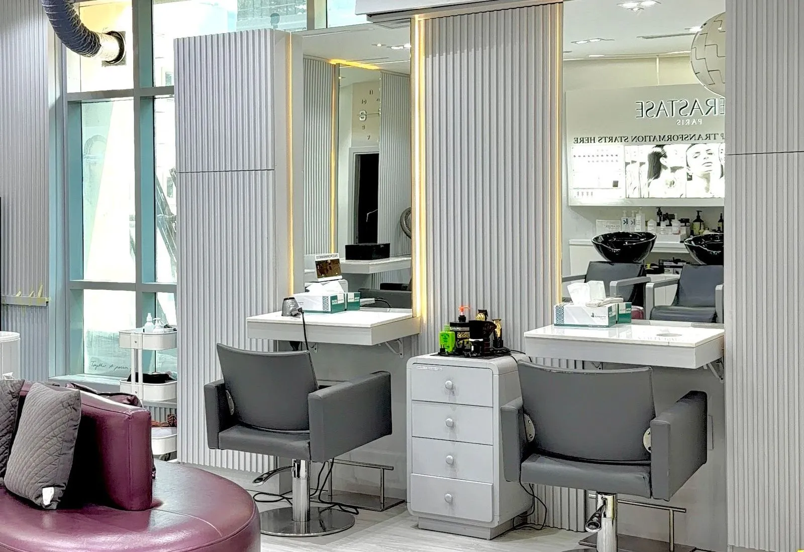 An empty hair salon with grey styling chairs, illuminated mirrors and a curved burgundy seat