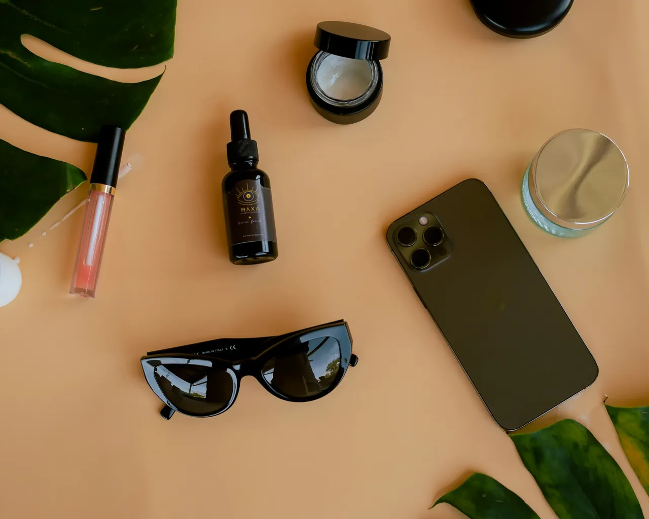 Skincare bottles, sunglasses and a phone arranged on a warm tabletop