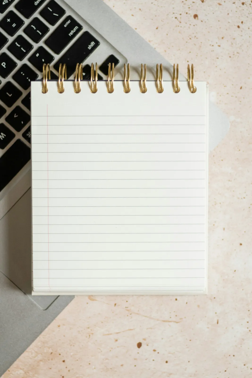 Lined notepad, spiral notebook and laptop keyboard on a pale desk