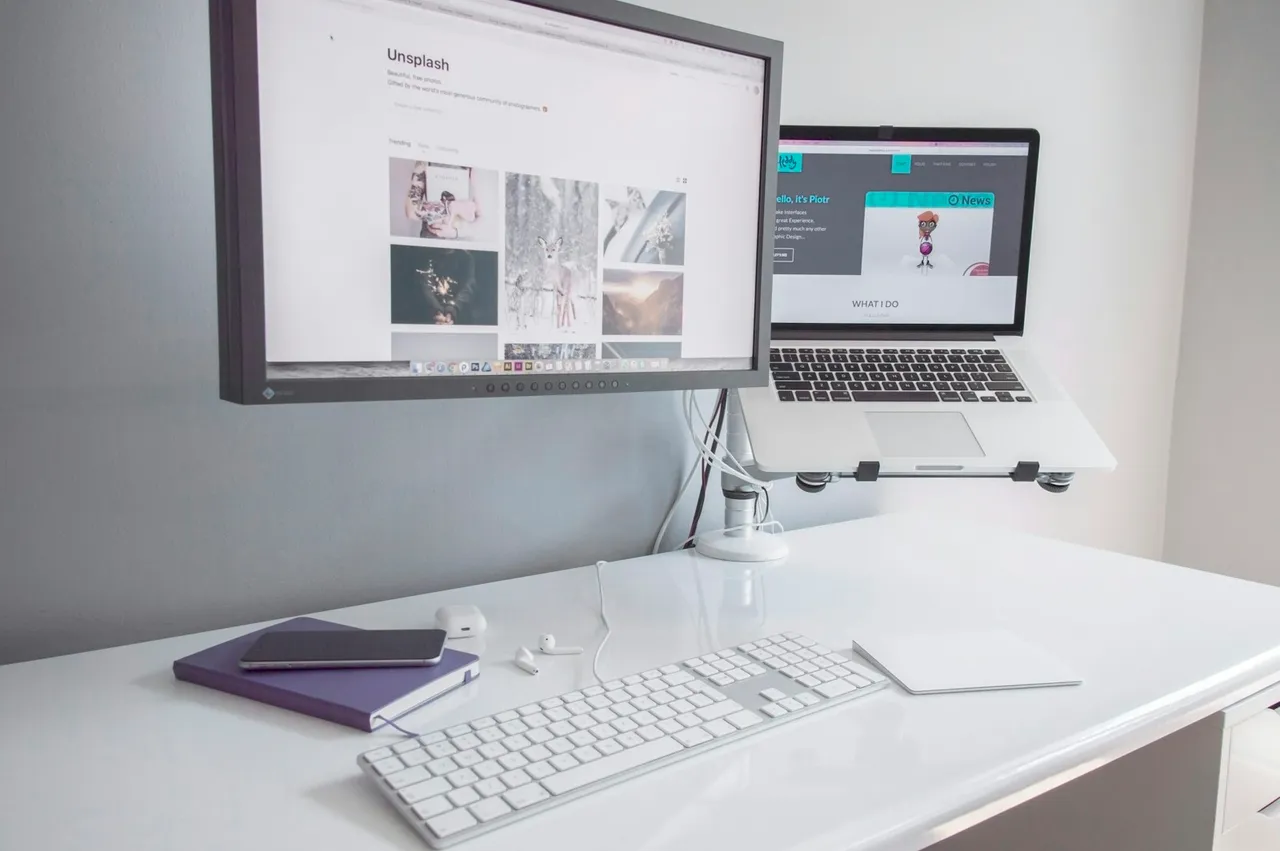 Flat screen monitor turned near MacBook Air turned on on white wooden table