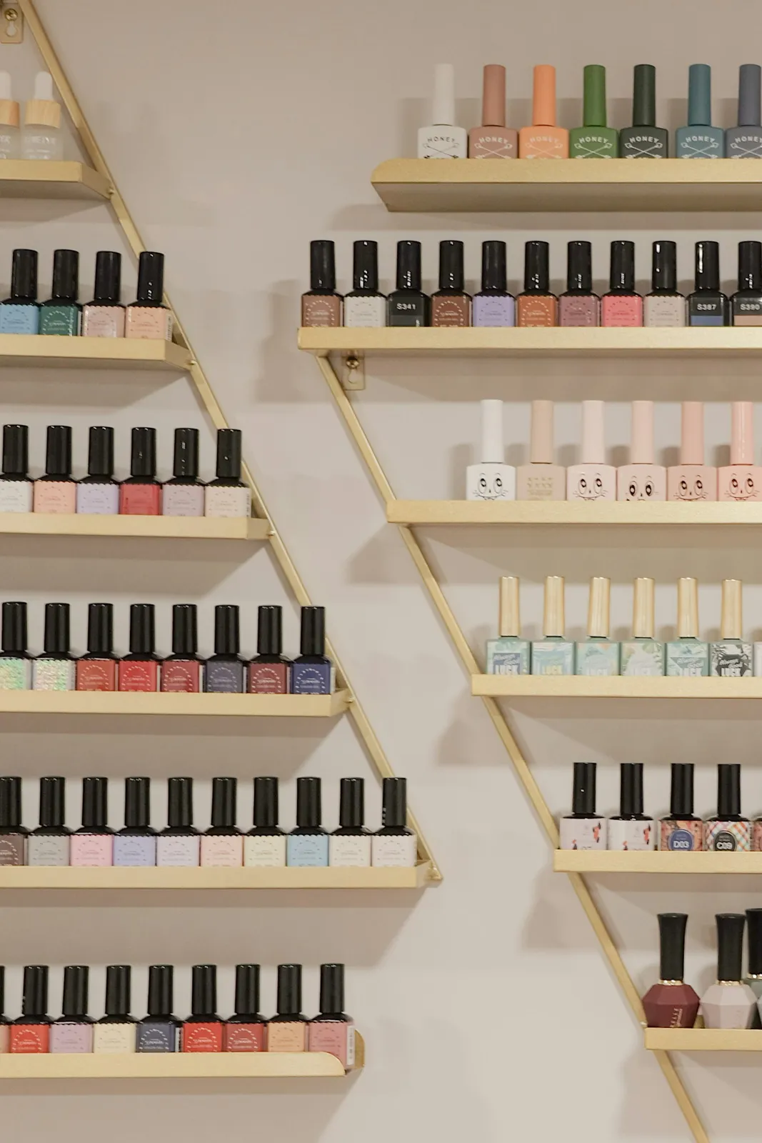 Rows of colorful nail polish bottles on gold triangular shelves against a wall